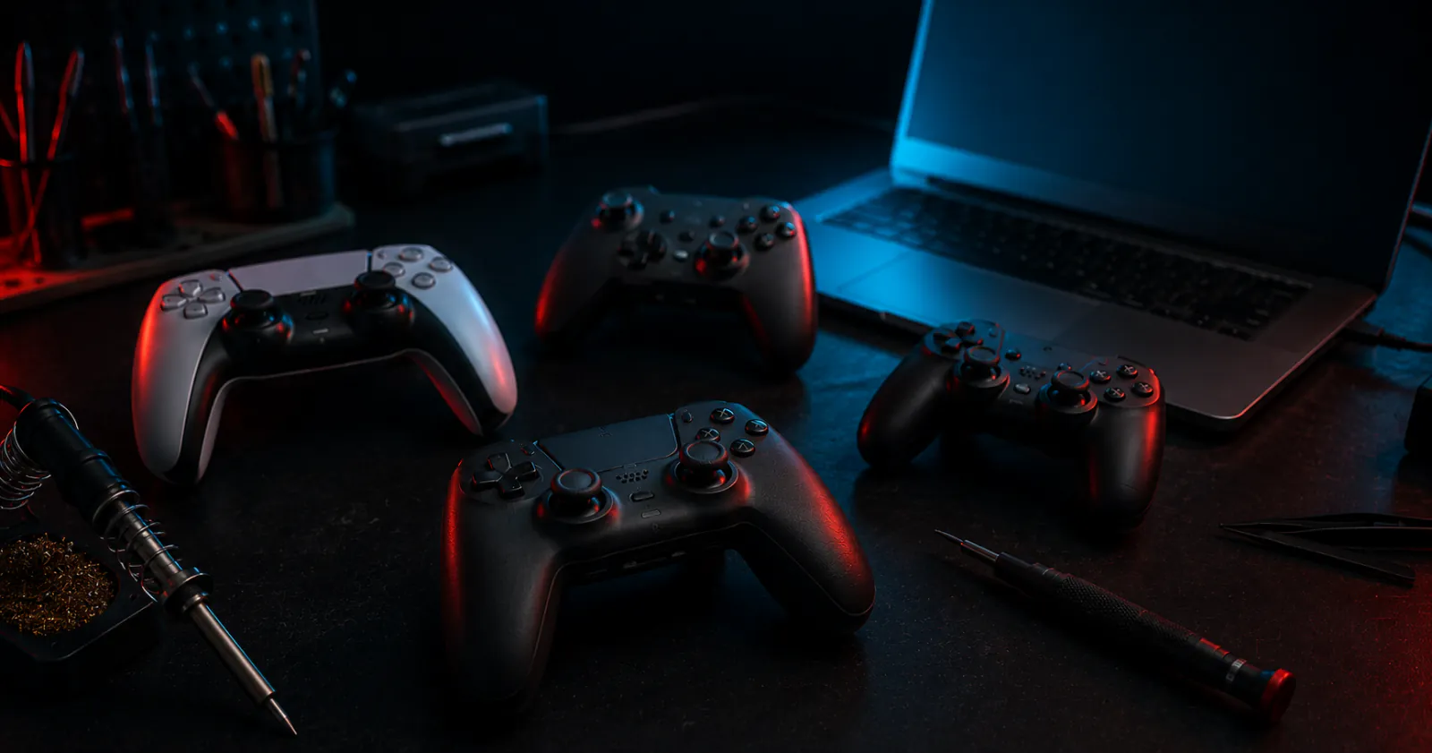 A repair desk with four game controllers opened for diagnosis beside tools, lit by a low workbench glow